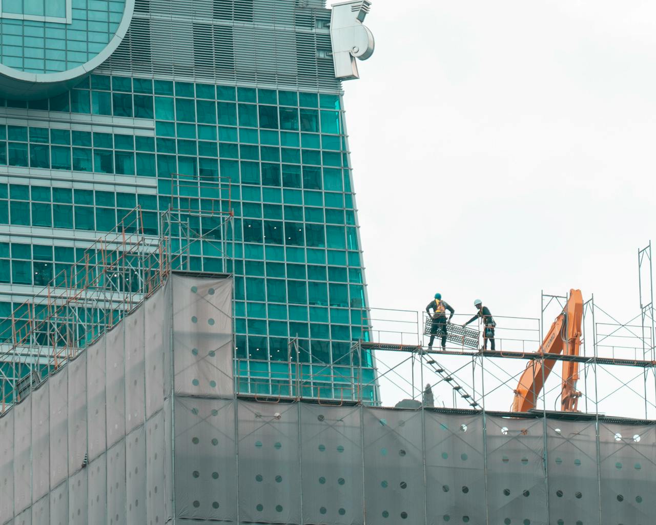 Two construction workers on scaffolding in front of a modern skyscraper under construction.