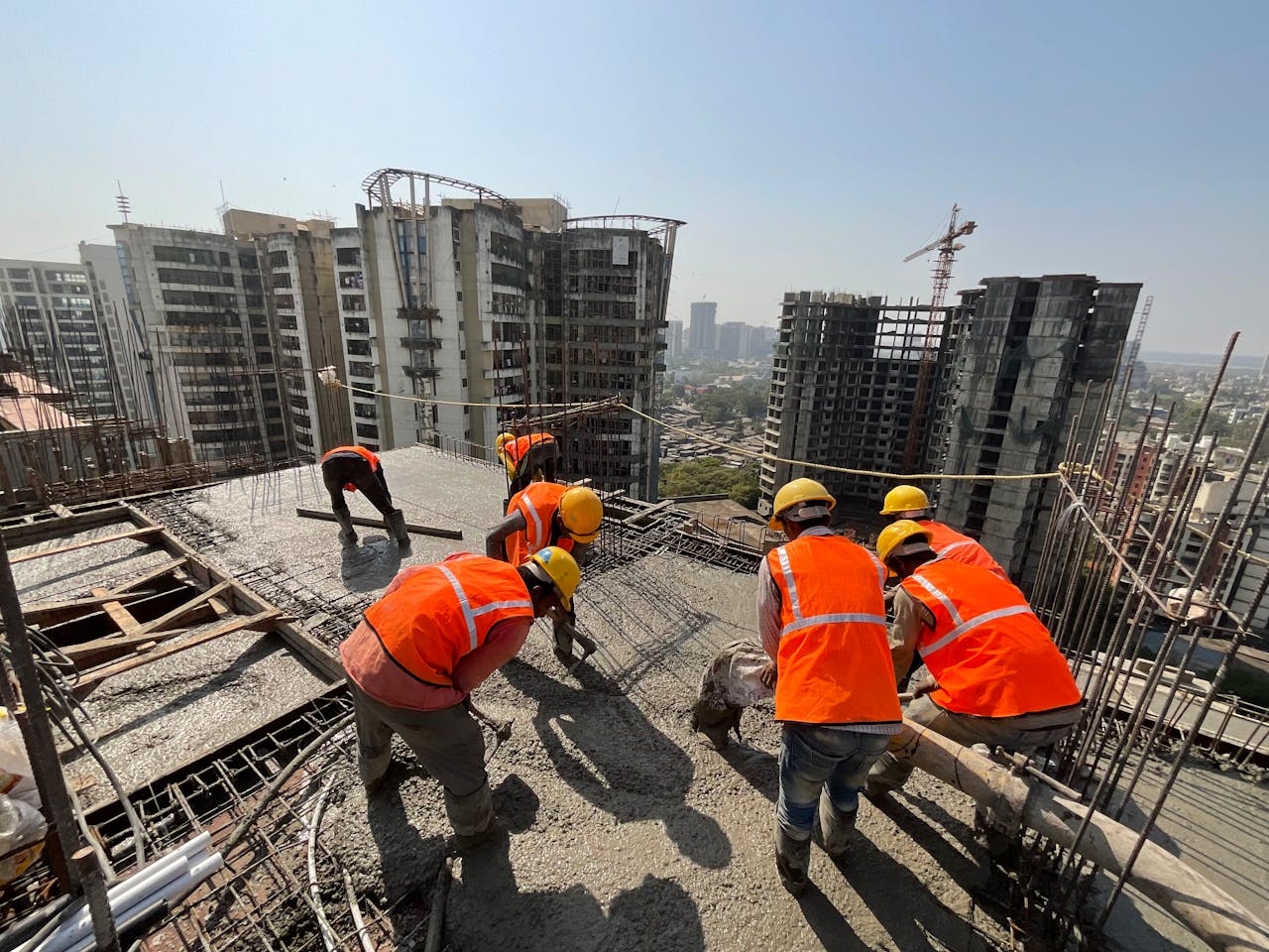 Workers in safety gear building a skyscraper with a city skyline backdrop.