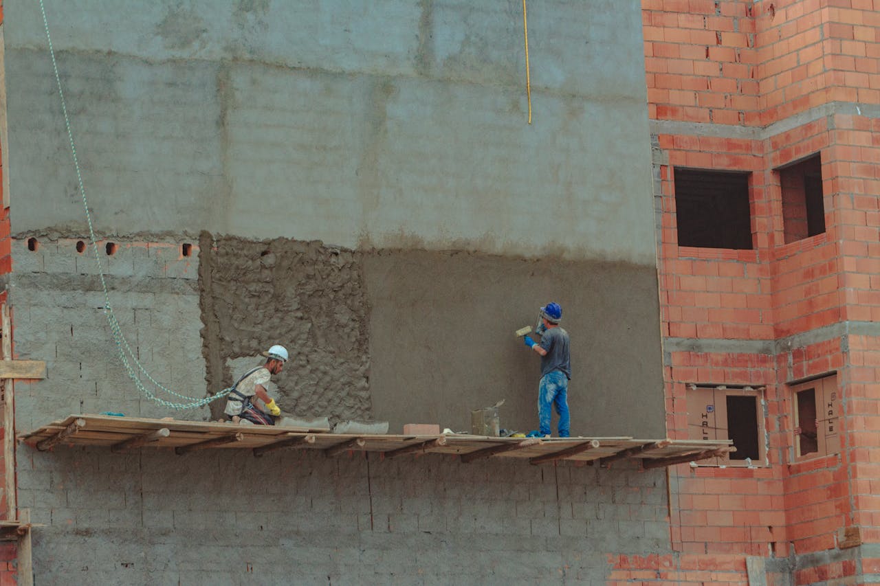Two construction workers plastering a brick wall on a building site.
