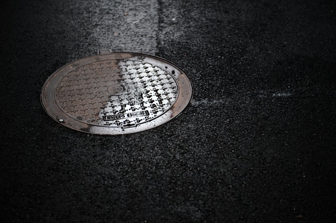 Close-up of a wet manhole cover on a rainy urban street, reflecting light.